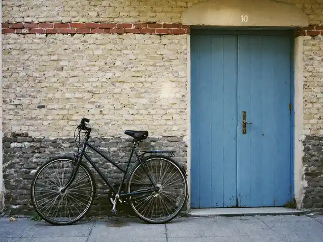 A bicycle leaning against a brick wall beside a closed blue door