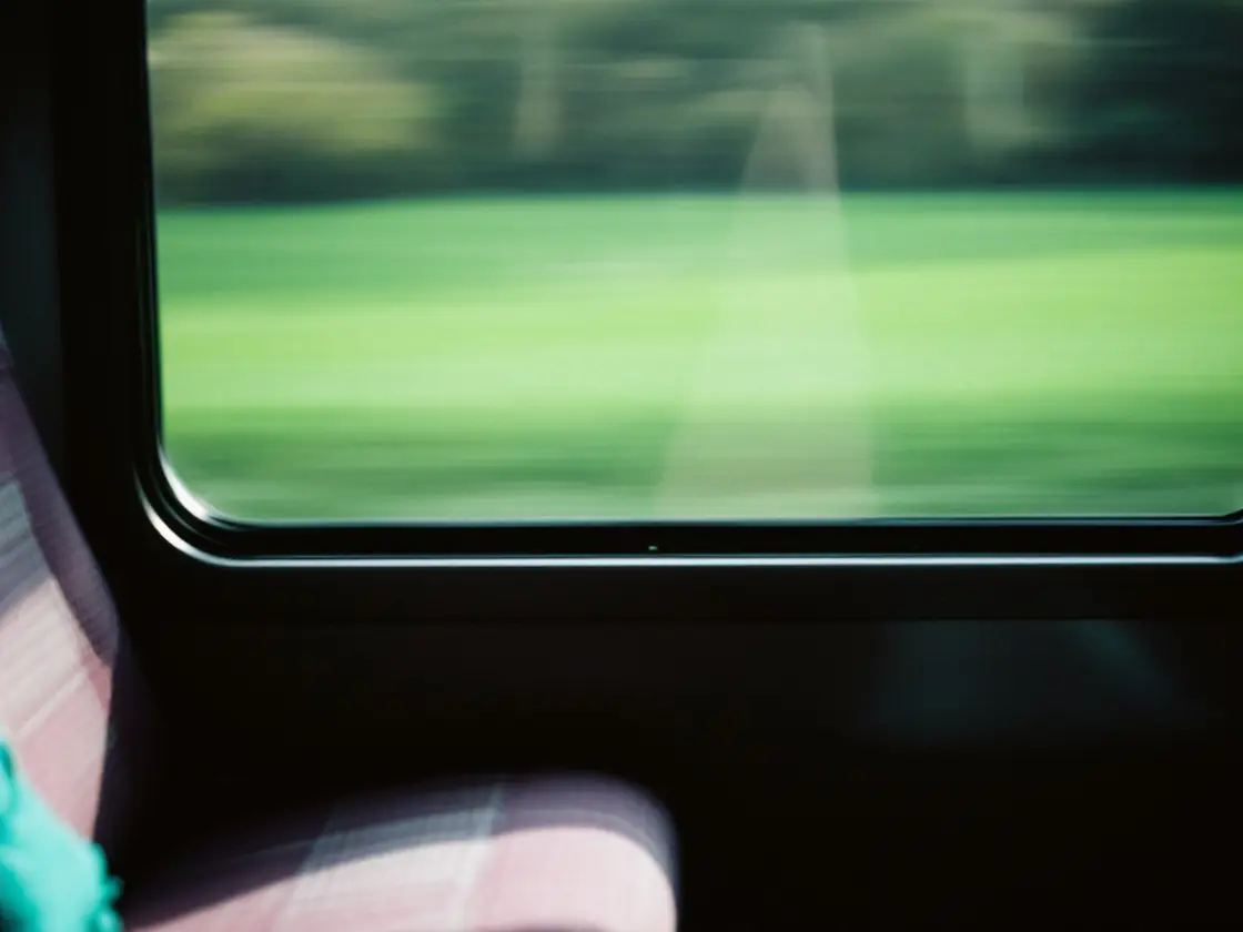 An empty train seat beside a window with green fields passing outside