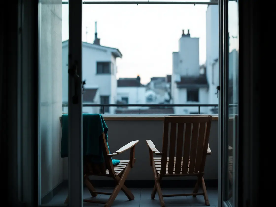 Two empty wooden chairs on a small balcony facing rooftops at dusk