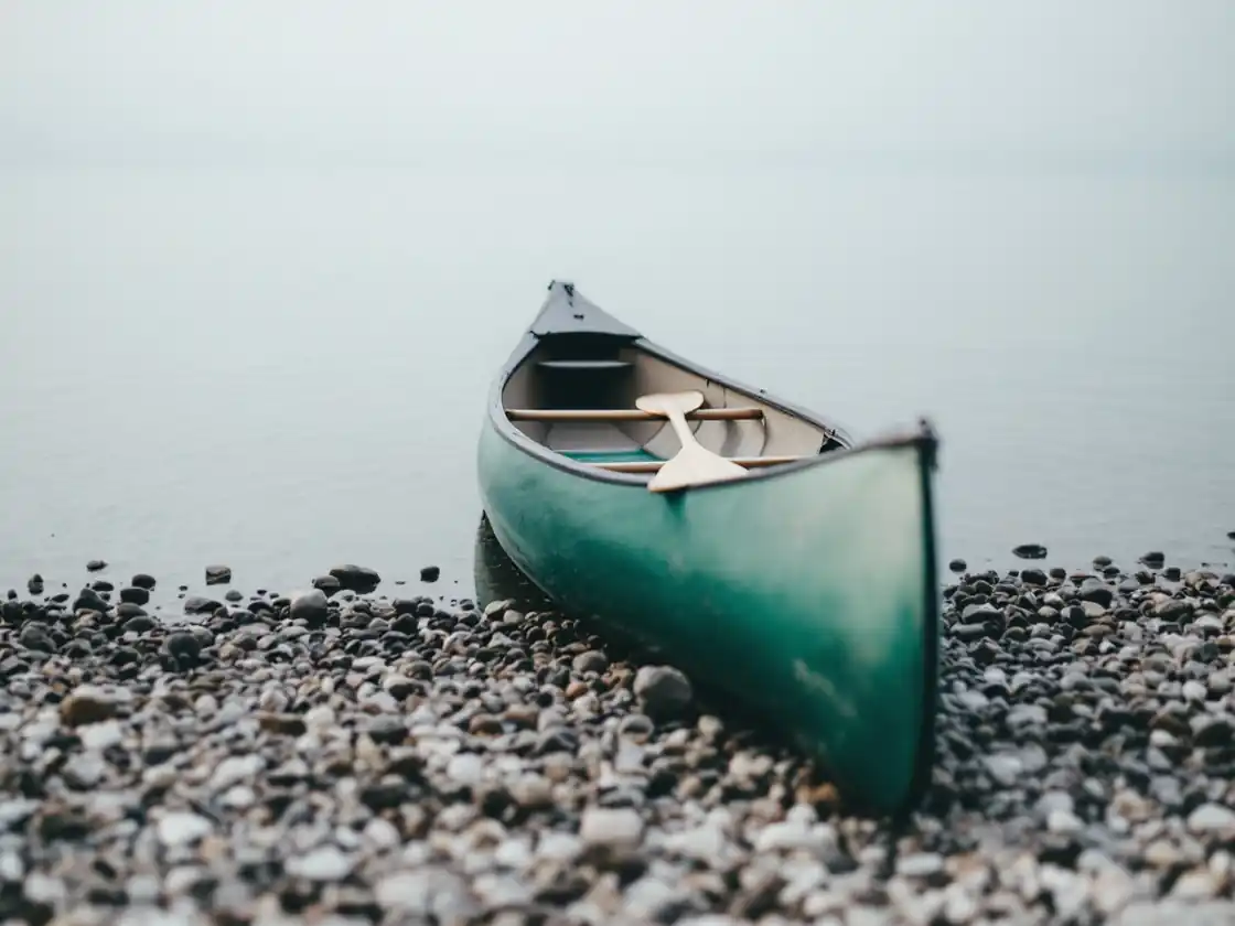 A green canoe pulled up on a pebble shore beside calm water