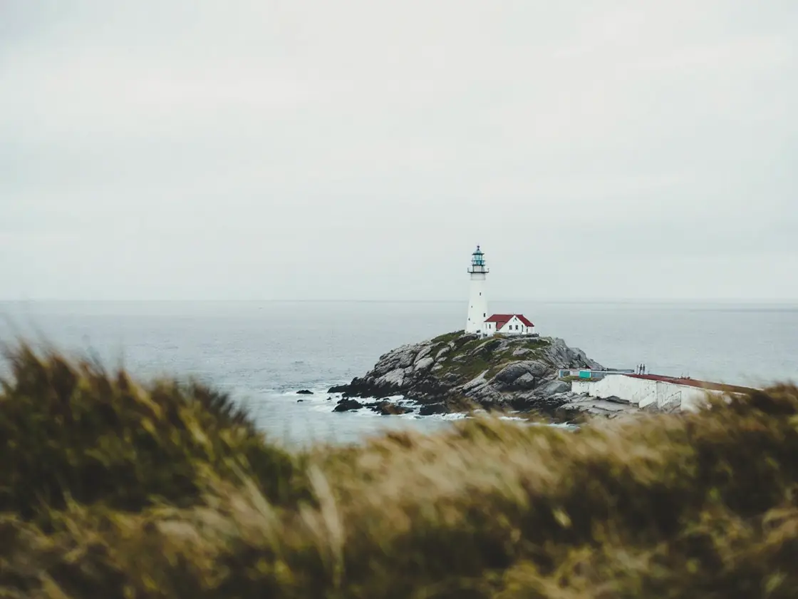 A white lighthouse on a rocky headland under an overcast sky