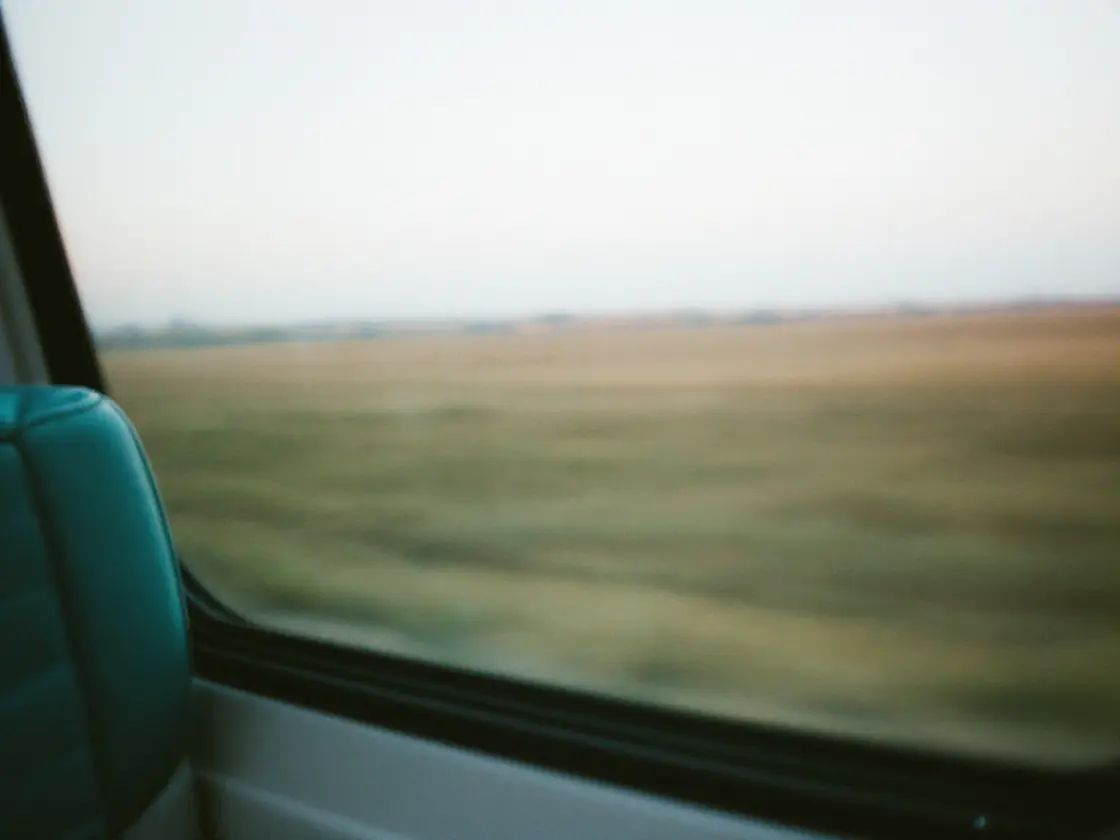 A train window with blurred fields and a pale sky outside