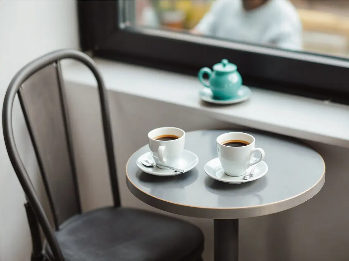 Two coffee cups on a small cafe table beside a window