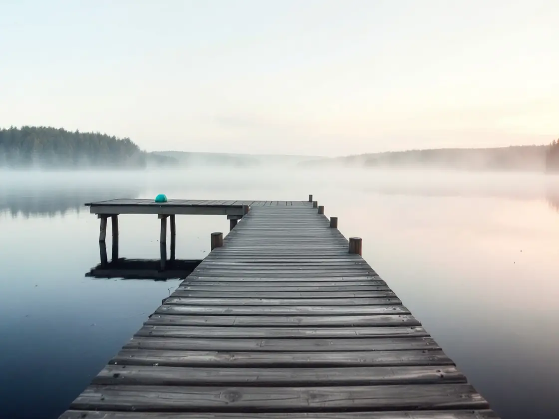 An empty wooden dock on a still misty lake at sunrise