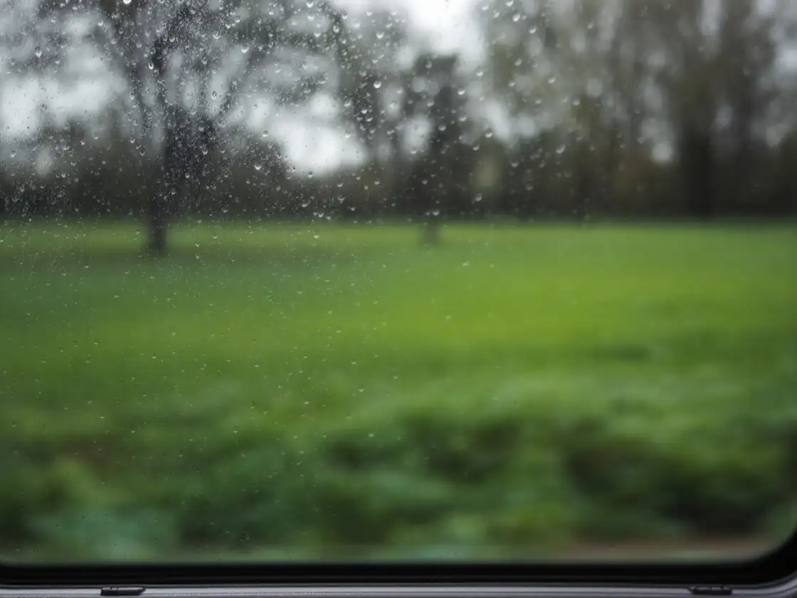 A rain-streaked train window with blurred green fields outside
