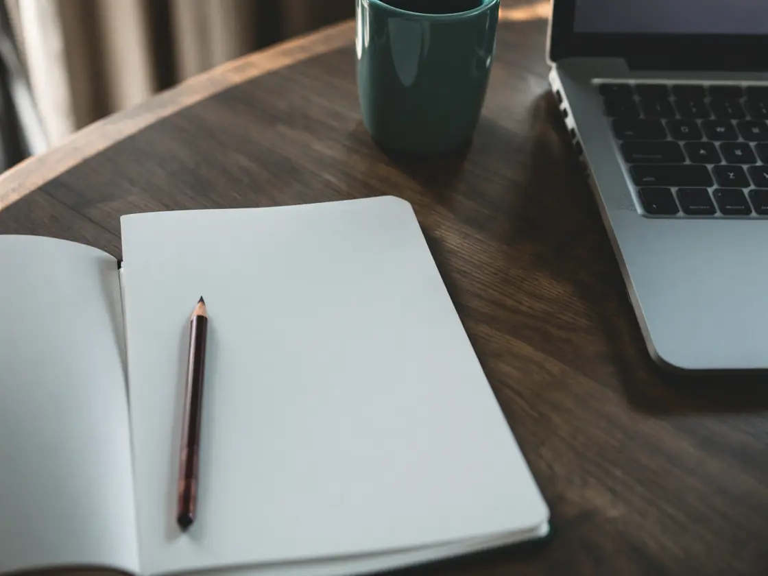 A wooden desk with an open notebook and a closed laptop