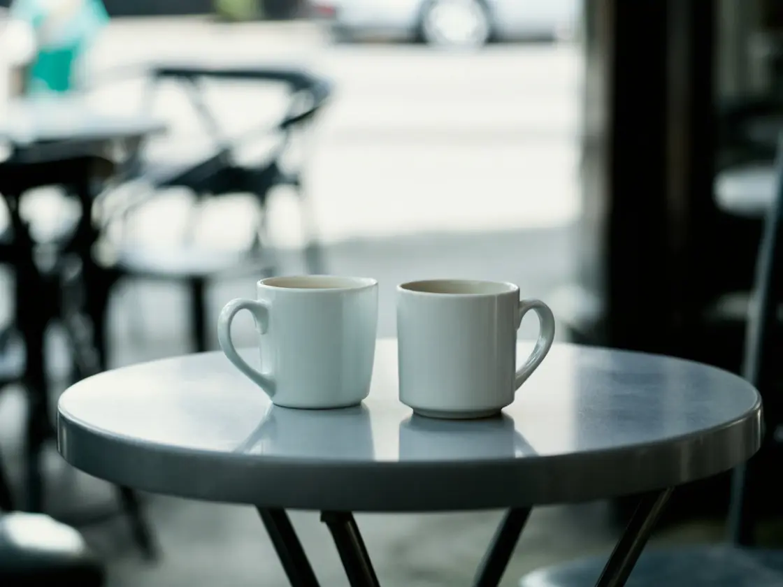 Two coffee cups on a small cafe table outside