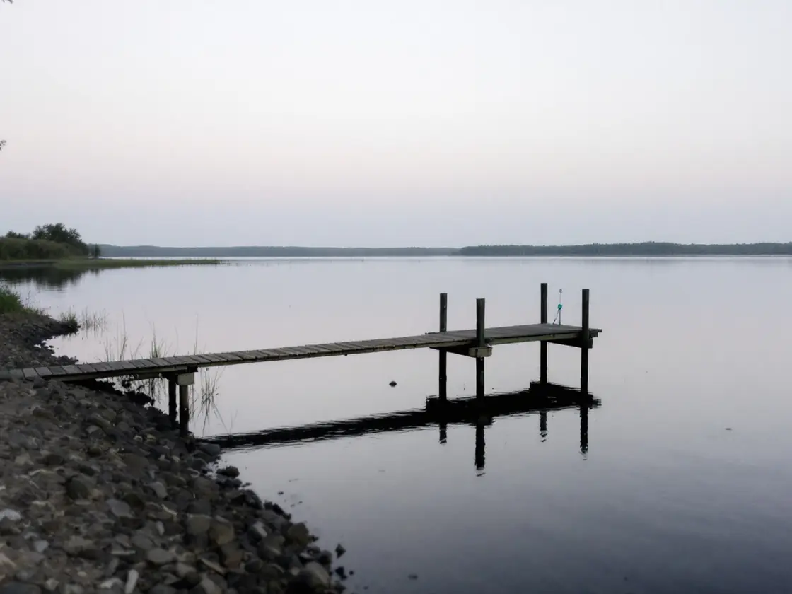 A lake shore at dusk with a wooden dock and still water