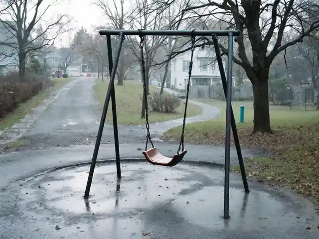 An empty playground swing set in a park on a gray morning
