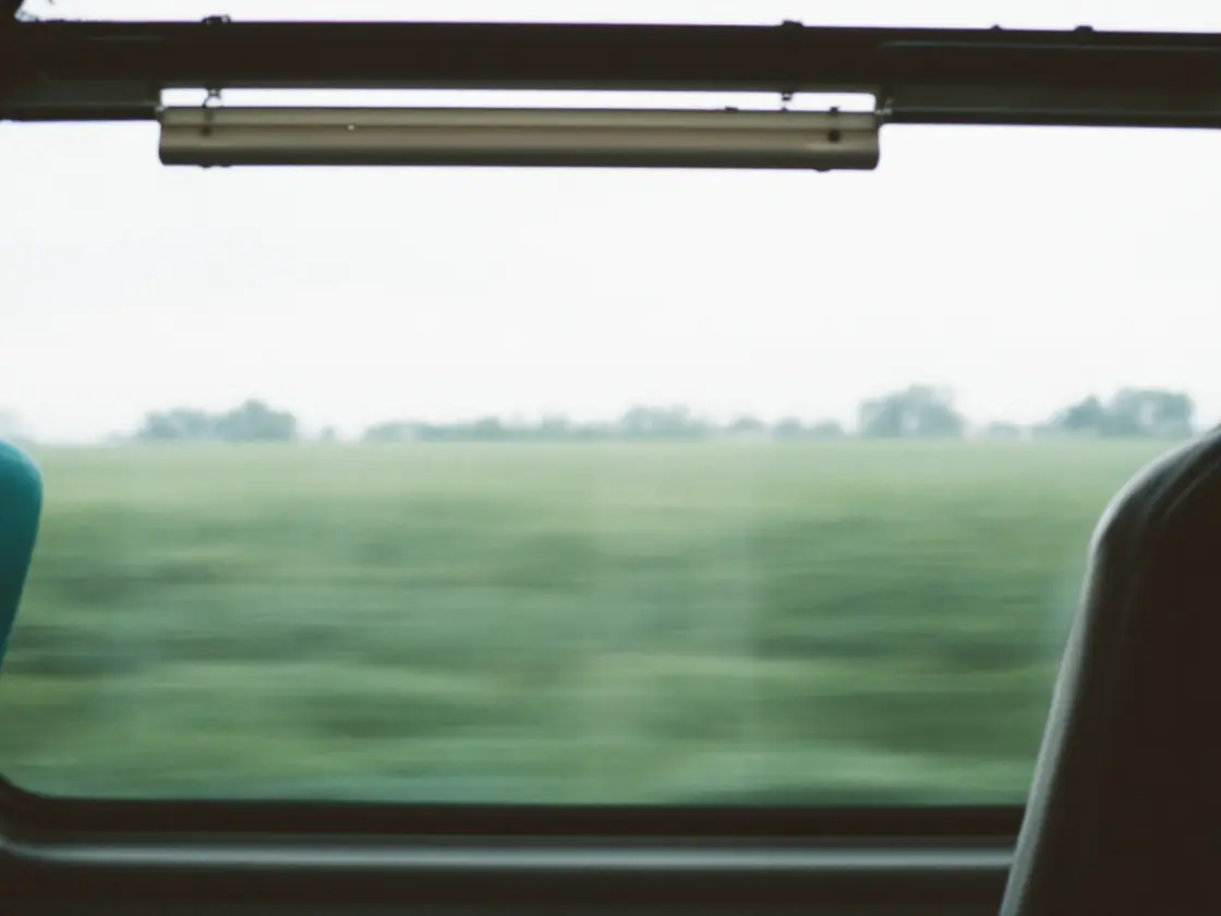 An empty train seat beside a window with fields passing outside
