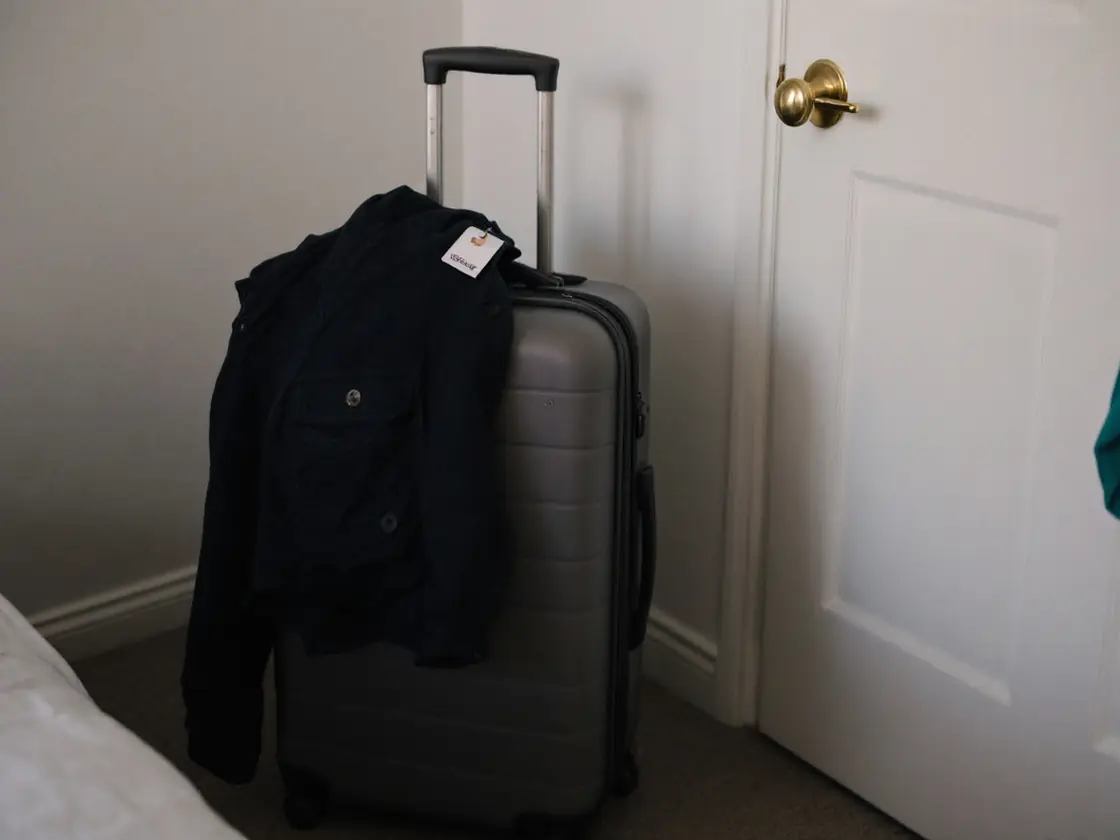 A small suitcase by a bedroom door with a jacket laid over it