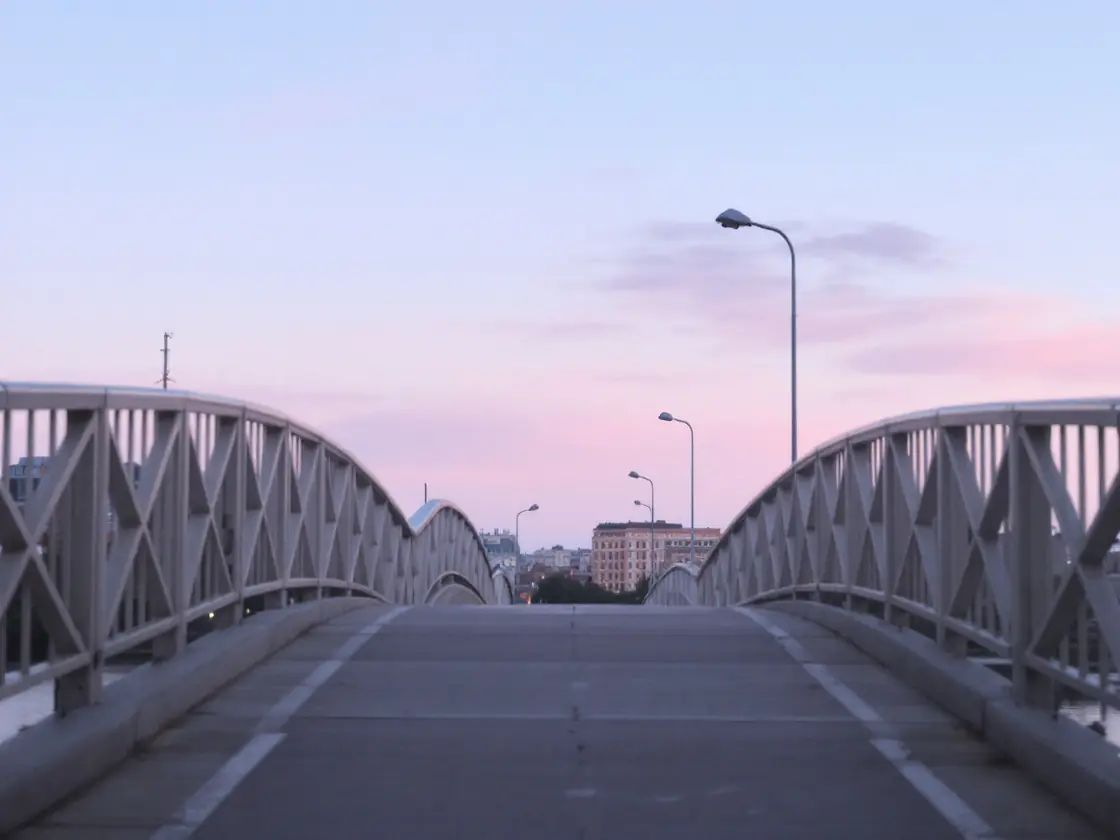 An empty footbridge over a river at sunrise under a pink sky