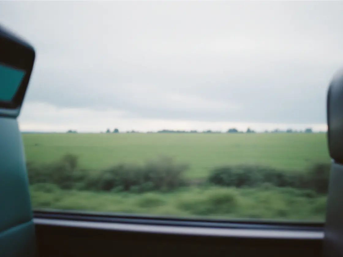 A train window view of fields passing under a cloudy sky