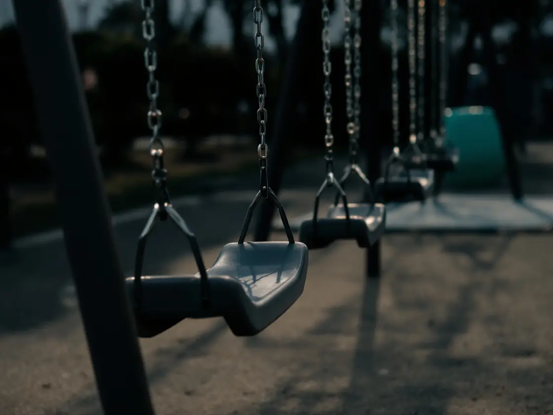 A row of empty swings in a playground at early evening