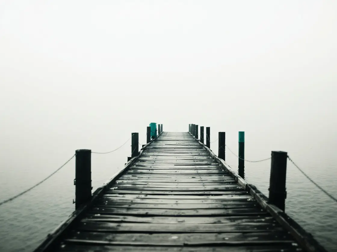 An empty pier stretching over calm water at sunrise with mist