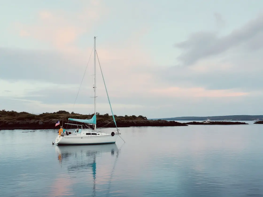 A small white sailboat anchored on a calm bay at sunrise